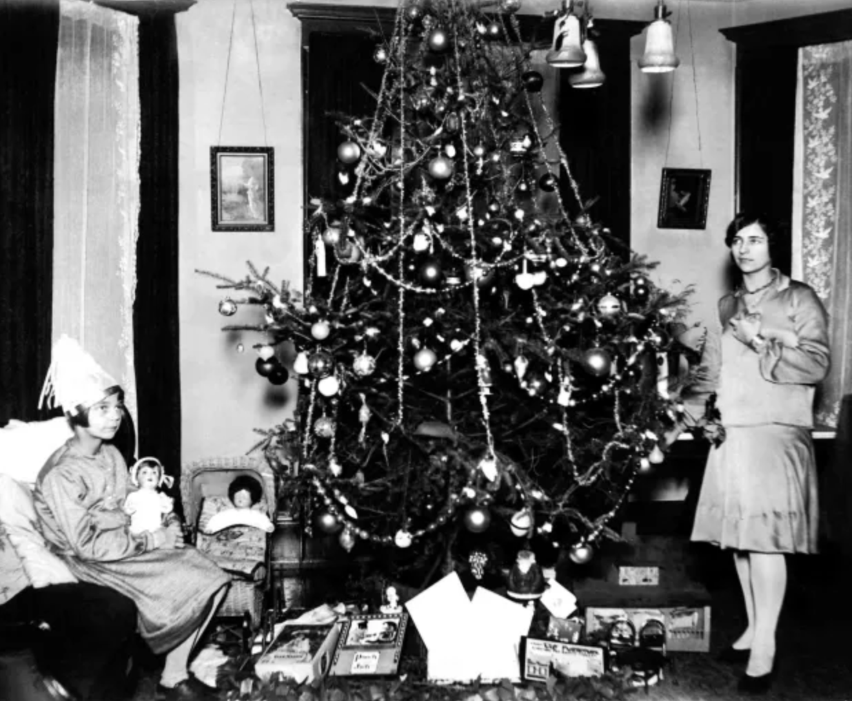 Two girls decorate a Christmas Tree with glass ornaments during the Art Deco era.